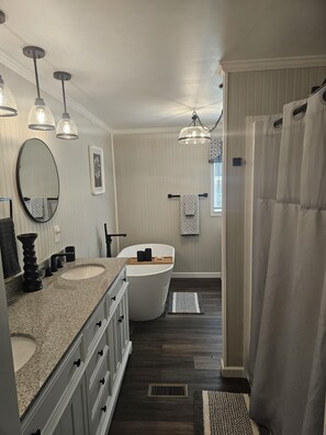 Un baño con tocador doble lavamanos, una bañera independiente y cortina de ducha.