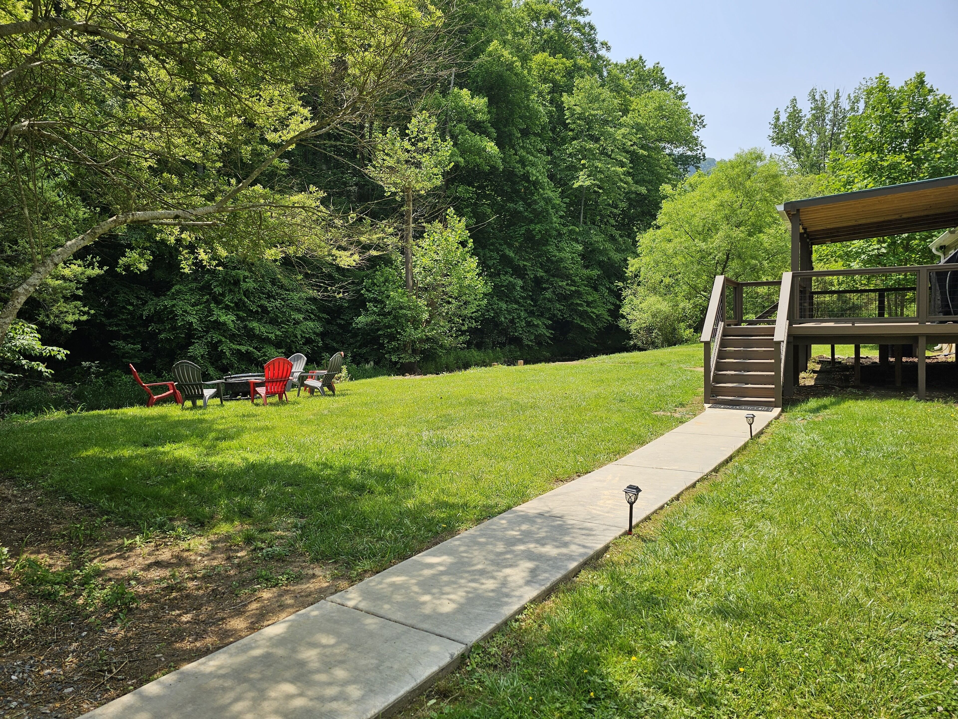 Un'area verde con prato, un vialetto in cemento che conduce a un pontile in legno e una zona coperta con sedute.