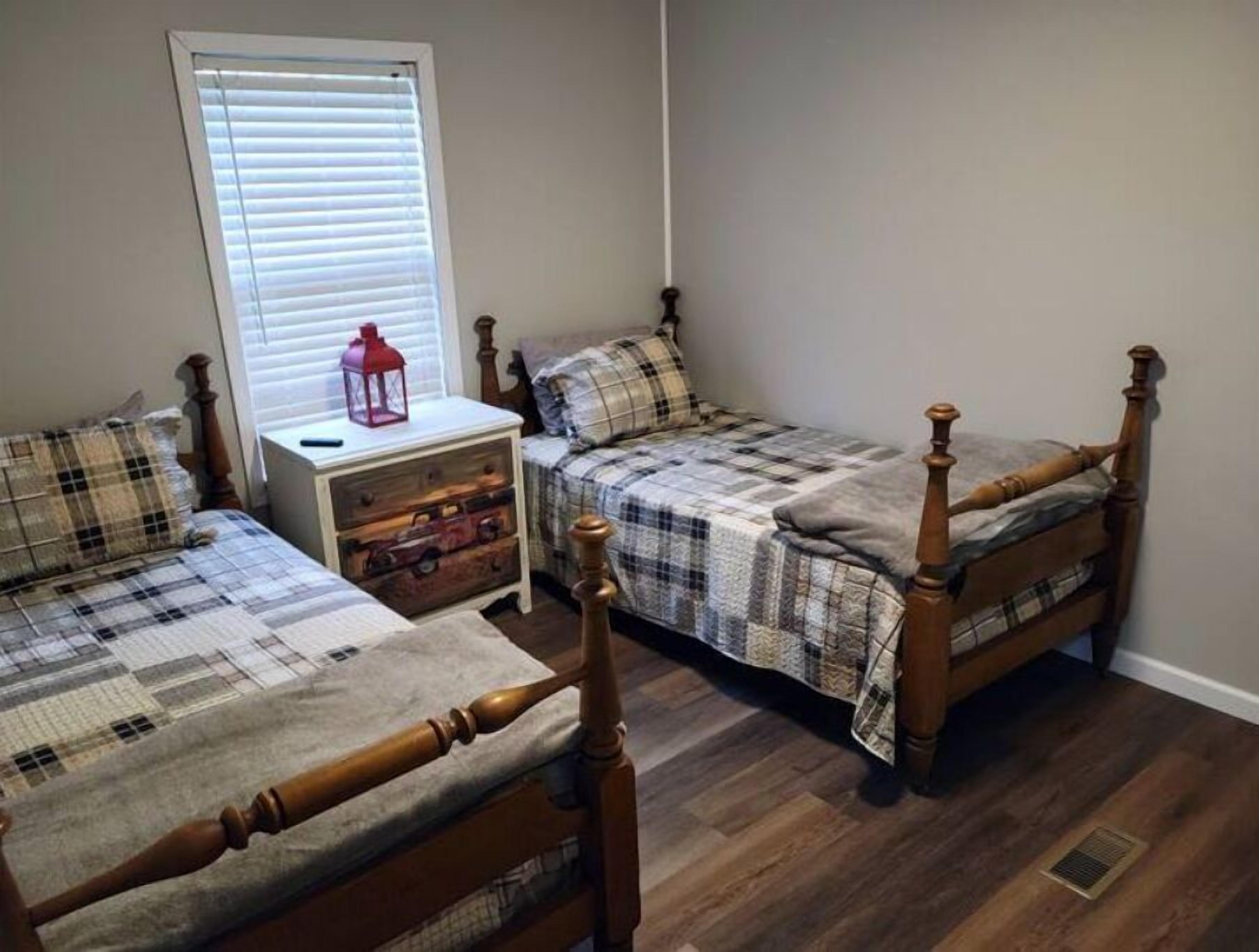 A bedroom with two wooden beds, a nightstand, and a window with blinds.