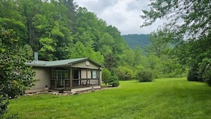 Une maison de plain-pied dotée d’un porche abrité, entourée d’une pelouse bien entretenue et d’une forêt dense.