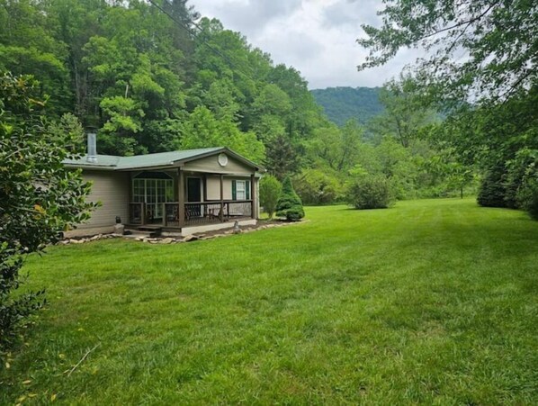 A single-story house with a covered porch, surrounded by a well-maintained lawn and dense forest.