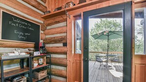 A log cabin interior with a welcome sign, wooden shelves, and a view of an outdoor patio with a table and umbrella.
