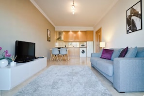 A modern living room with a flat-screen TV, a grey sofa, and a dining area with chairs.