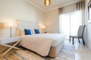Une chambre d’hôtel avec un grand lit, des lampes de chevet, un fauteuil et une vue sur l’extérieur.