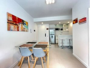 Una cocina moderna con armarios blancos, un refrigerador y un microondas. Hay un comedor con una mesa y sillas.