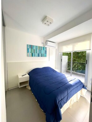 Un dormitorio con cama, mesita de noche, aire acondicionado de pared y ventana con vistas a zonas verdes.