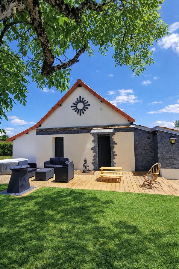 A modern house with a sun motif on the facade, a wooden deck, outdoor seating, and a statue.