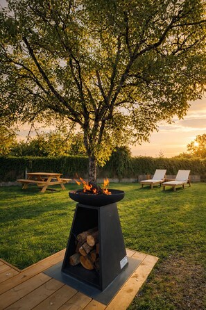 An outdoor patio area with a fire pit, lounge chairs, and a wooden table.