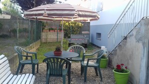 Un patio con mesa y sillas, un paraguas a rayas y una parrilla.