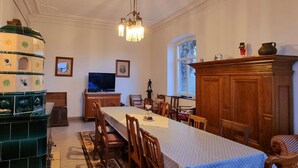 A dining room with a long table, chairs, a chandelier, a television, and a decorative stove. - Das Alte Herrenhaus - Wohnen wie zu Kaisers Zeiten (Kevelaer)