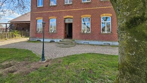 A red brick building with multiple windows and a door, surrounded by a gravel path and greenery. - Das Alte Herrenhaus - Wohnen wie zu Kaisers Zeiten (Kevelaer)