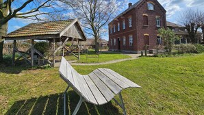 A rustic building with a red brick facade, a wooden bench, and a gazebo in a grassy area. - Das Alte Herrenhaus - Wohnen wie zu Kaisers Zeiten (Kevelaer)