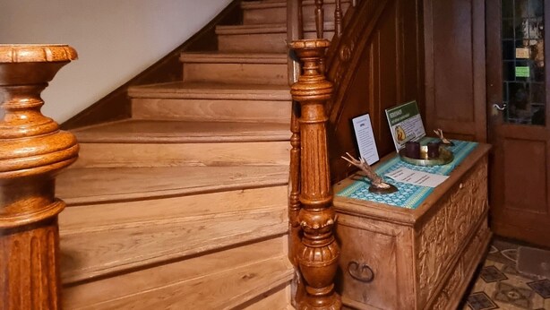 A wooden staircase with a handrail and a small table with a menu at the bottom. - Das Alte Herrenhaus - Wohnen wie zu Kaisers Zeiten (Kevelaer)