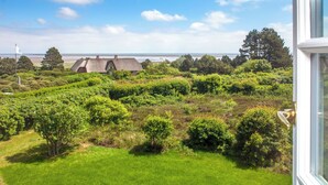 A coastal landscape with a grassy area, trees, and a building with a thatched roof.