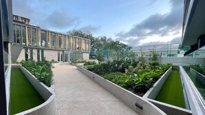 Un edificio moderno con fachada de vidrio, un camino central y áreas ajardinadas con plantas verdes.