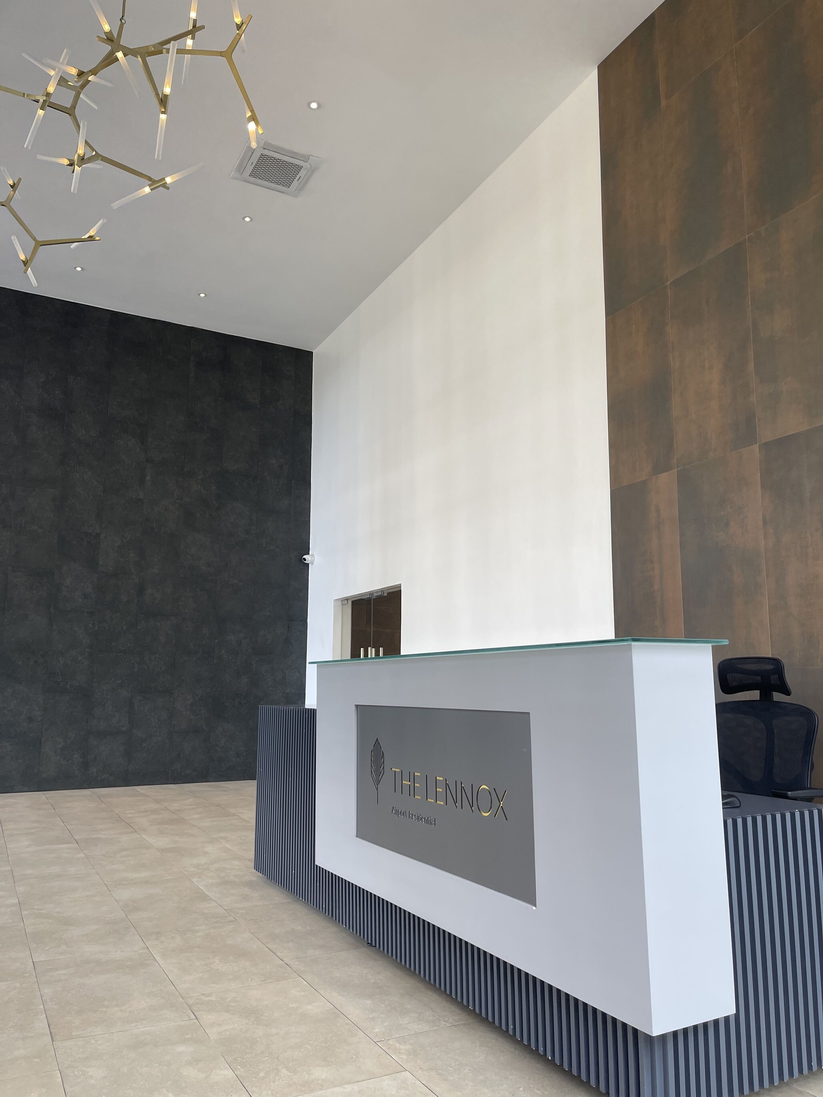 Un comptoir d’accueil moderne, doté d’un plateau en verre et arborant le logo « THE LENNOX ».