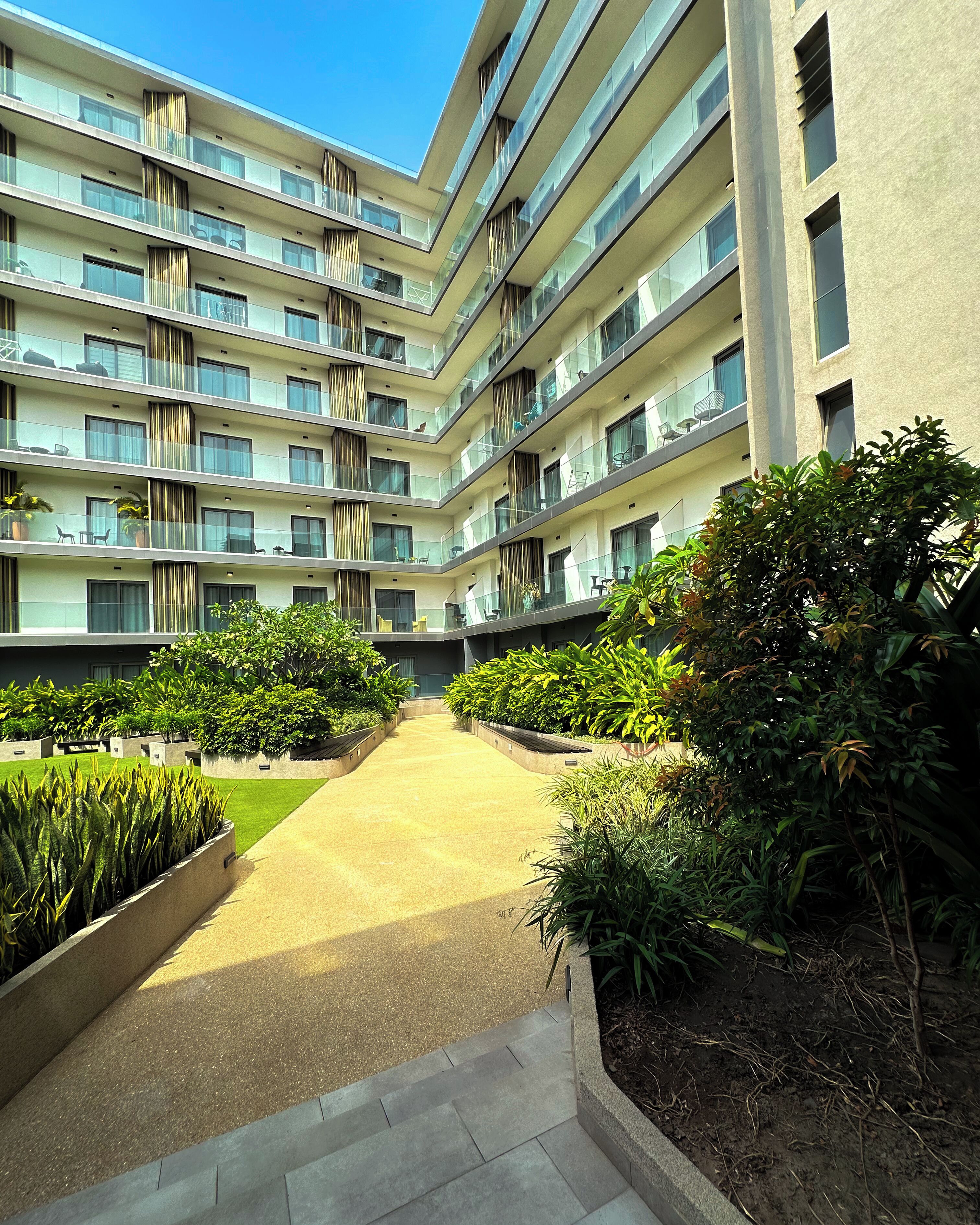 A multi-story building with balconies, a central pathway, and surrounding greenery.
