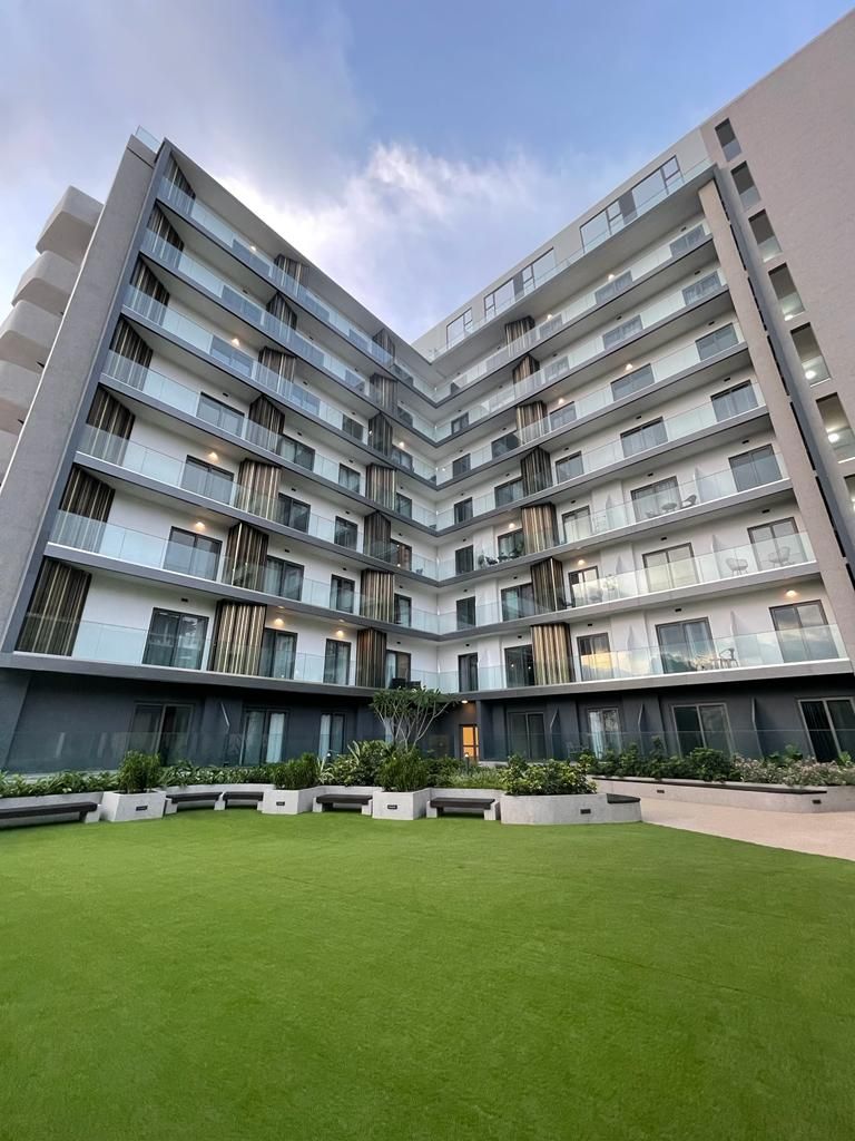 A multi-story building with balconies, a well-maintained lawn, and a clear sky.