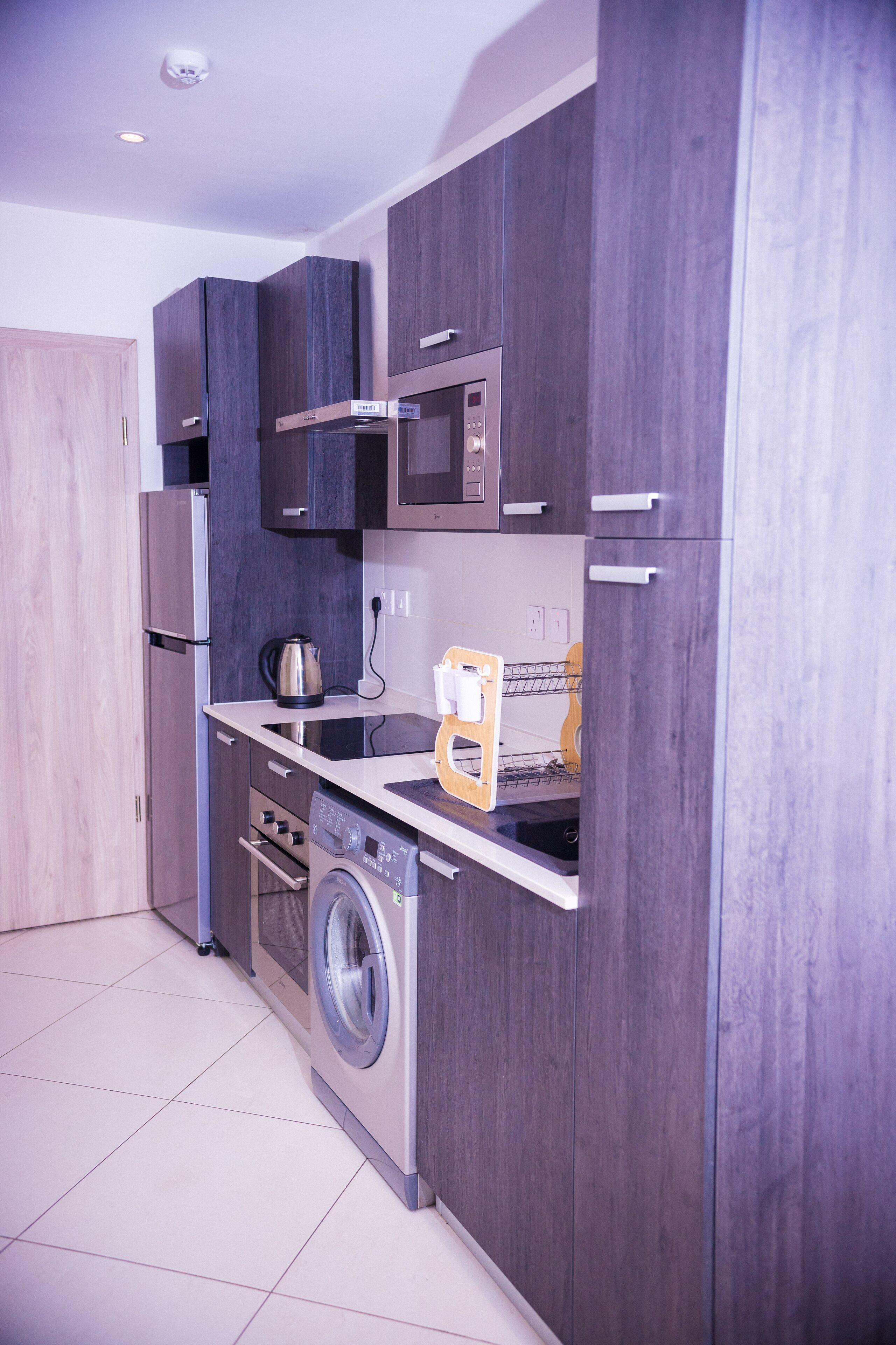 A compact kitchen with a microwave, kettle, and washing machine.