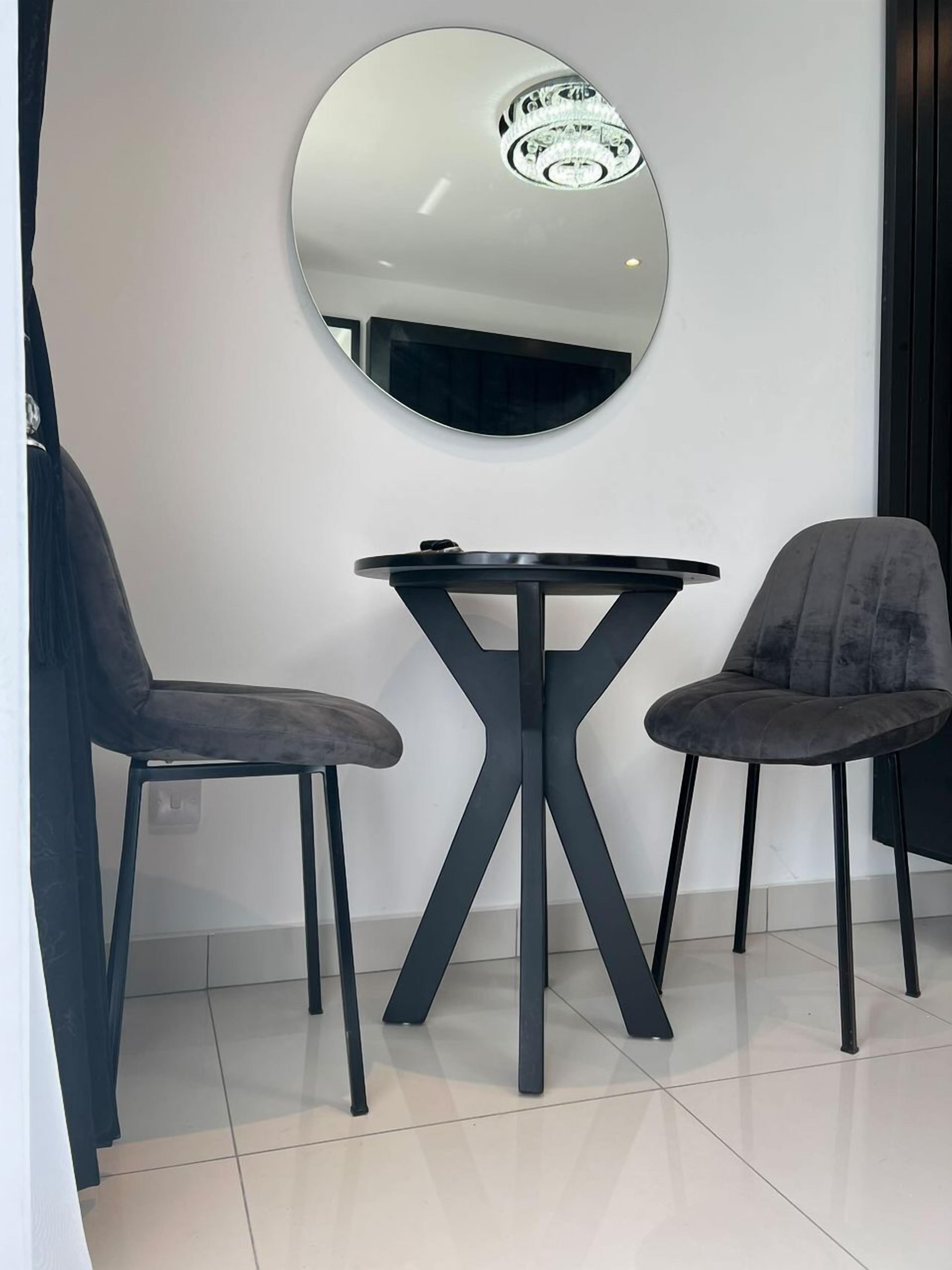 A modern room with a round mirror, two black chairs, and a small table.