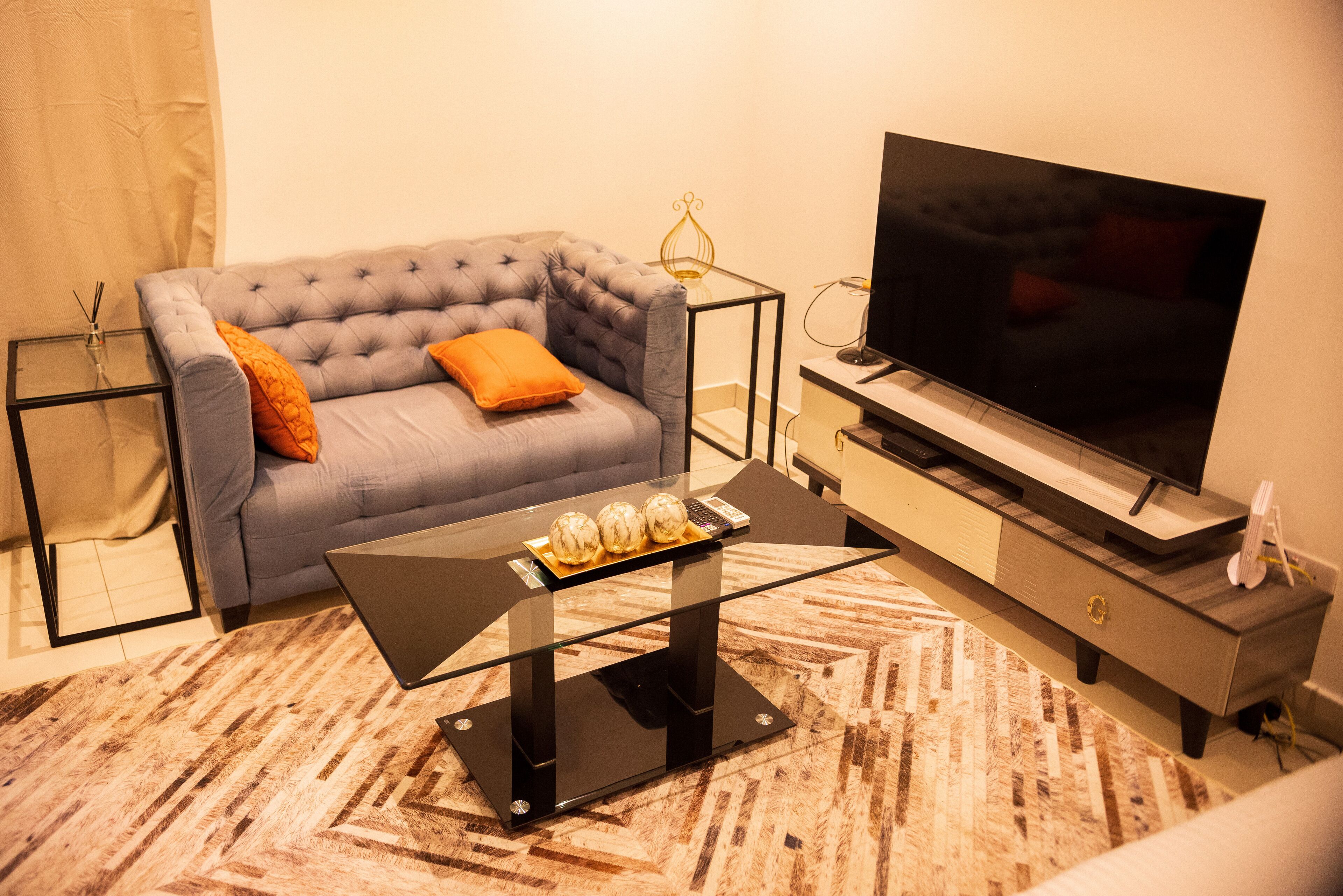 Un soggiorno moderno con un divano grigio, un tavolino in vetro, una TV a schermo piatto e un tappeto fantasia.
