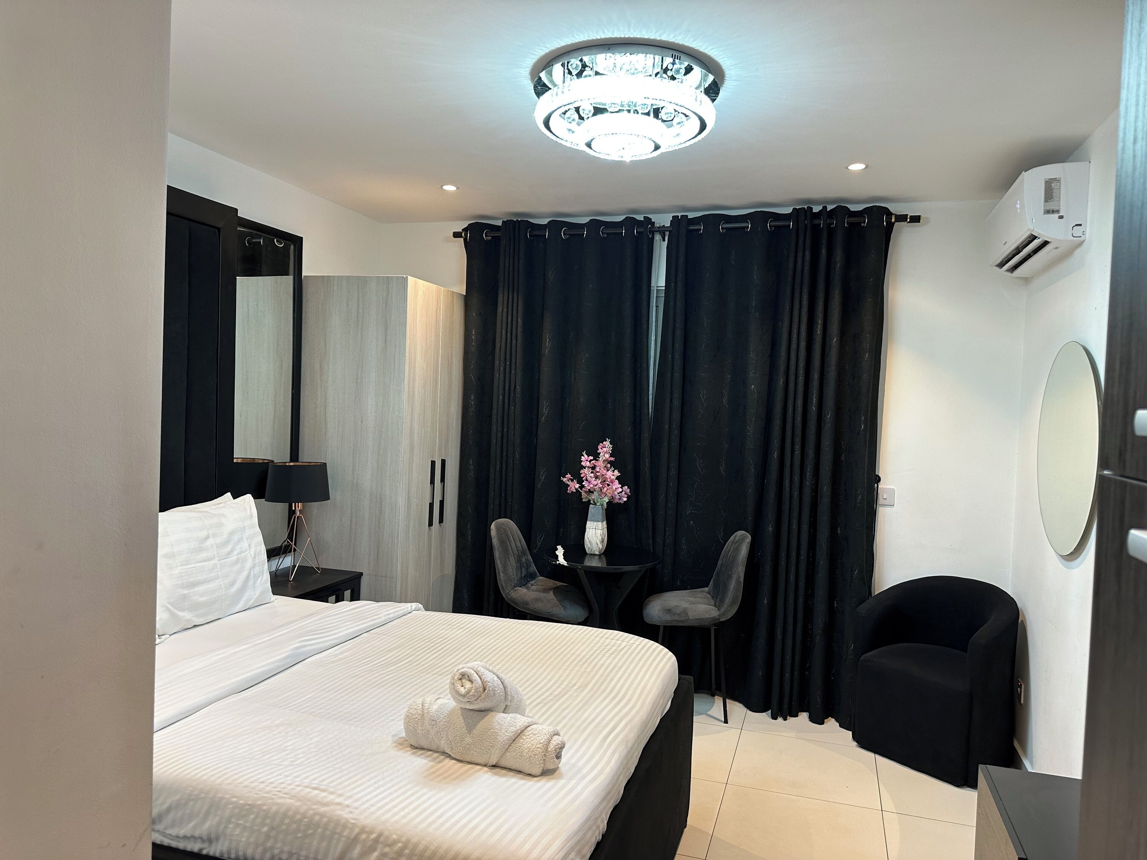 A hotel room with a bed, a desk, two chairs, a mirror, and a ceiling light fixture.