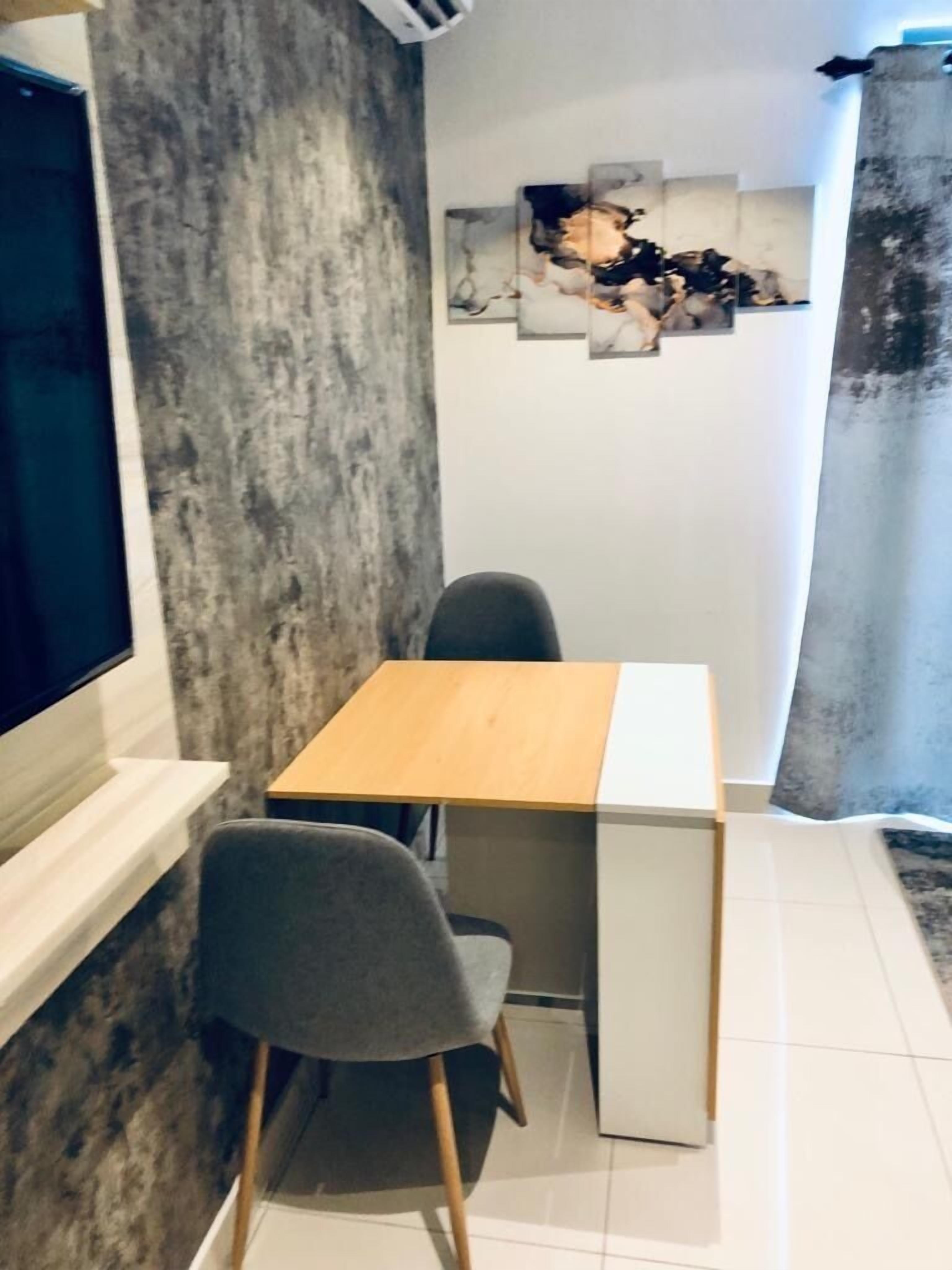 A small, modern room with a wooden desk and two chairs, a large window, and a textured wall.
