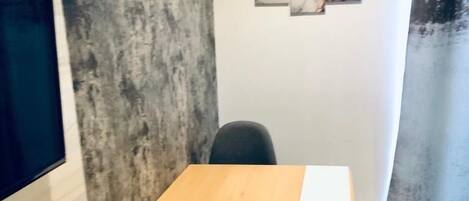 A small, modern room with a wooden desk and two chairs, a large window, and a textured wall.