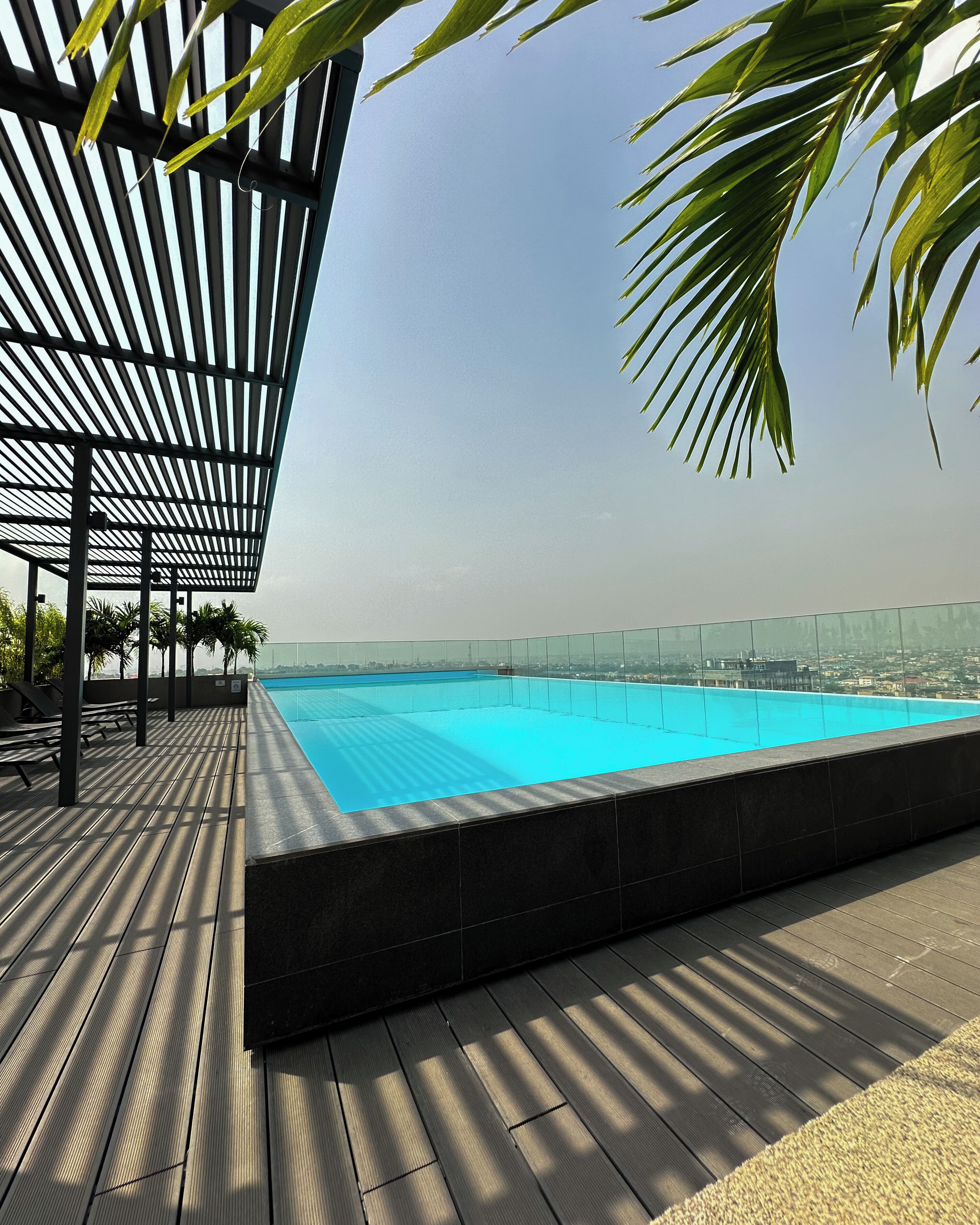 Piscina no terraço com deck de madeira e guarda-corpo de vidro.