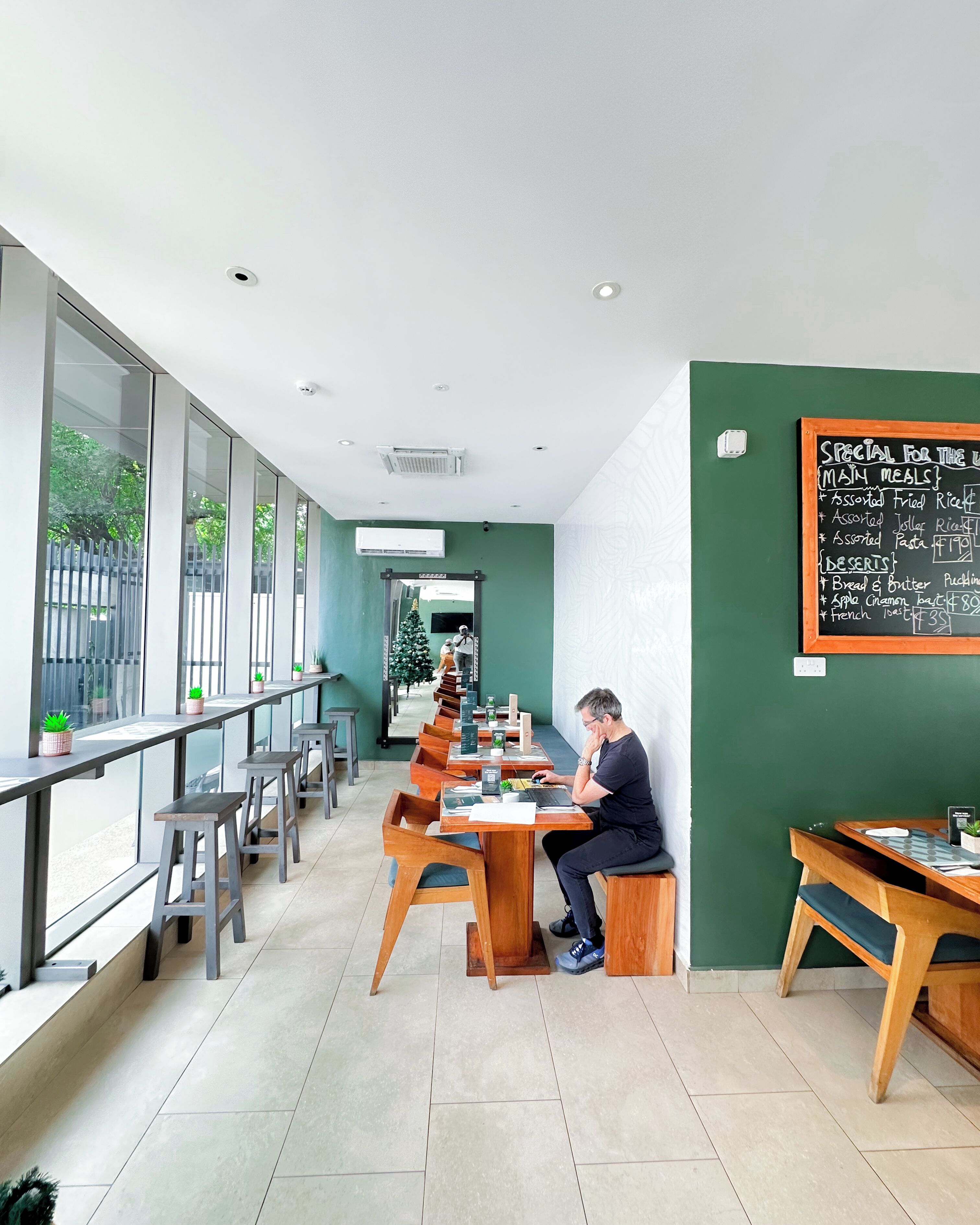 A modern restaurant with long communal tables, individual seating, and a chalkboard menu.