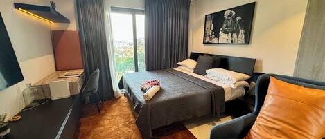 Quarto de hotel com cama, escrivaninha, cadeira, sofá e um quadro na parede.