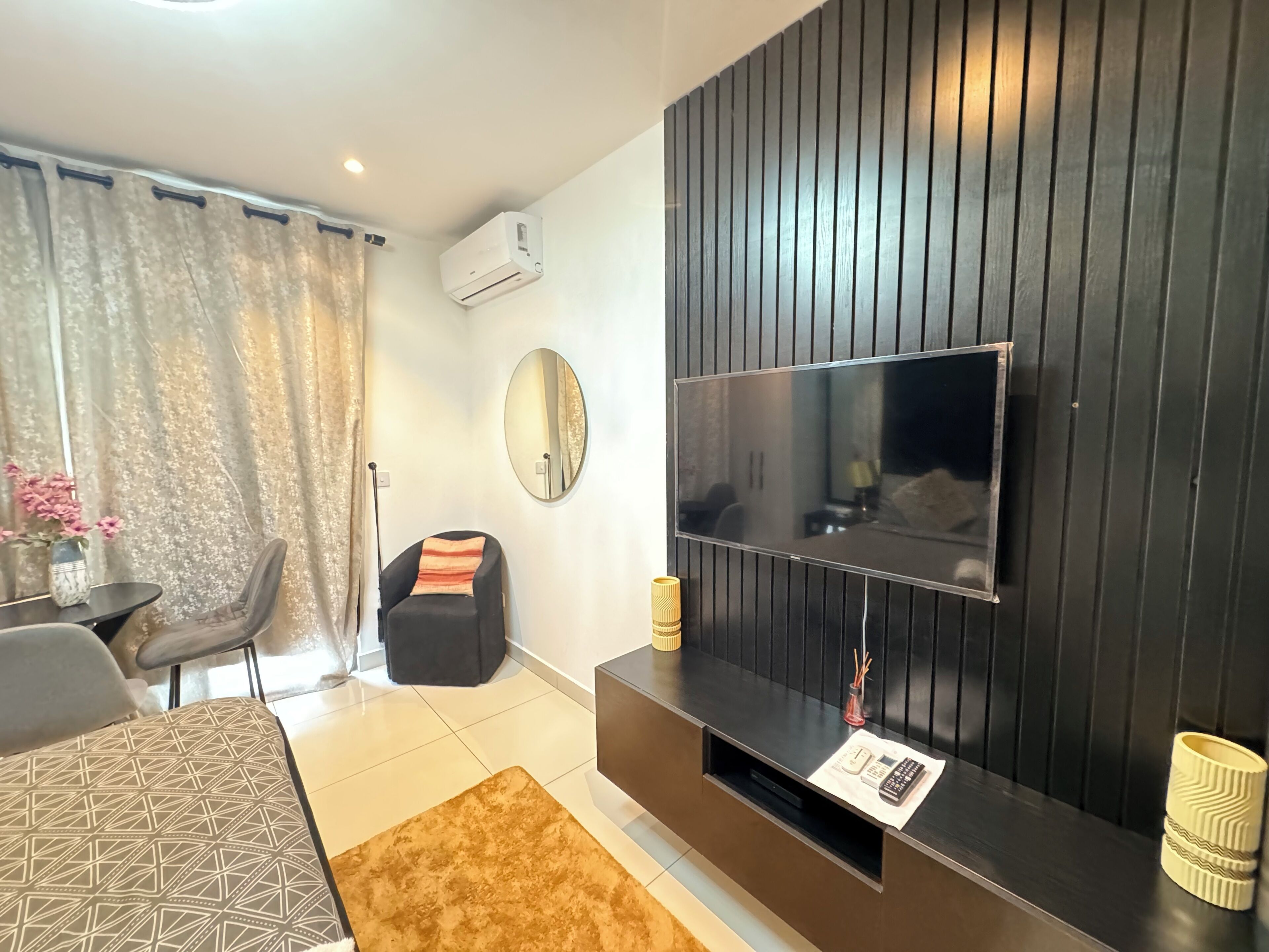 A modern living room with a flat-screen TV, a sofa, a dining table, and a decorative mirror.