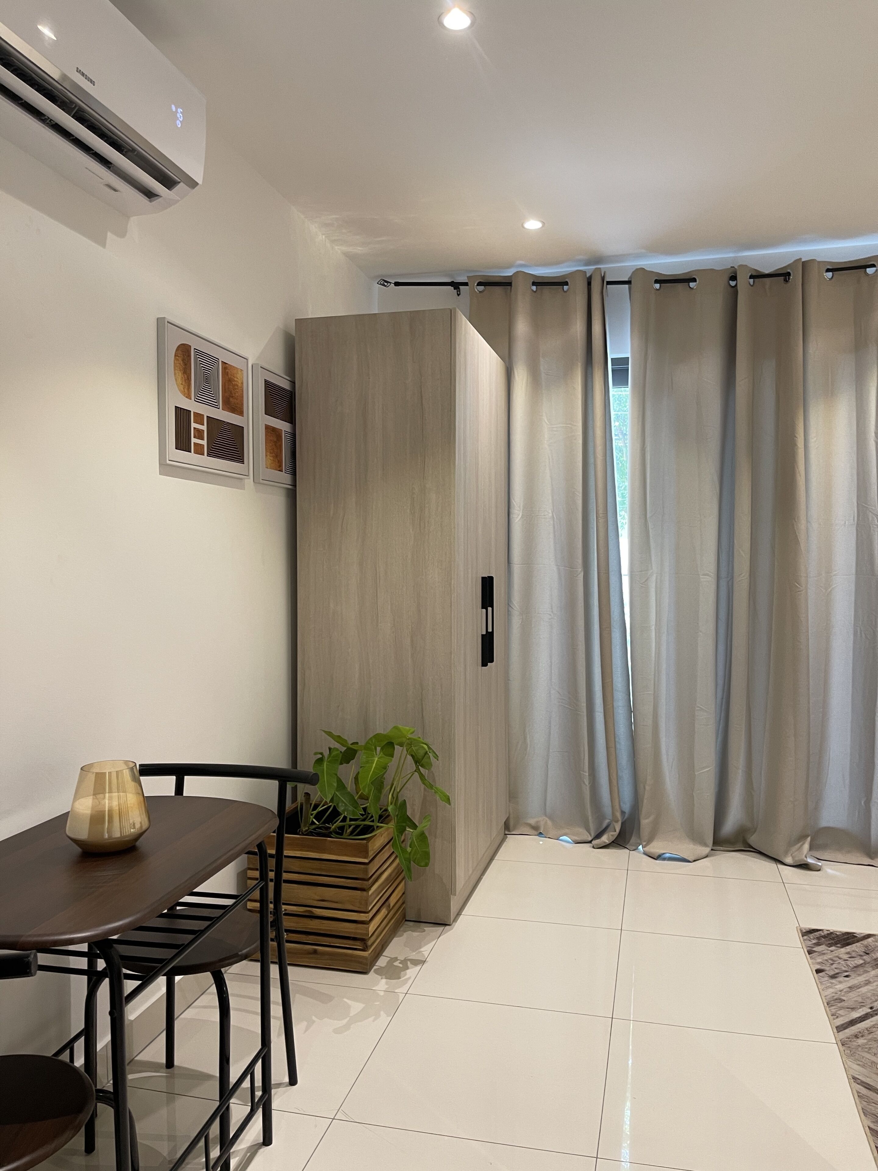 A modern living room with a dining table, chairs, a potted plant, a cabinet, and a large window with curtains.