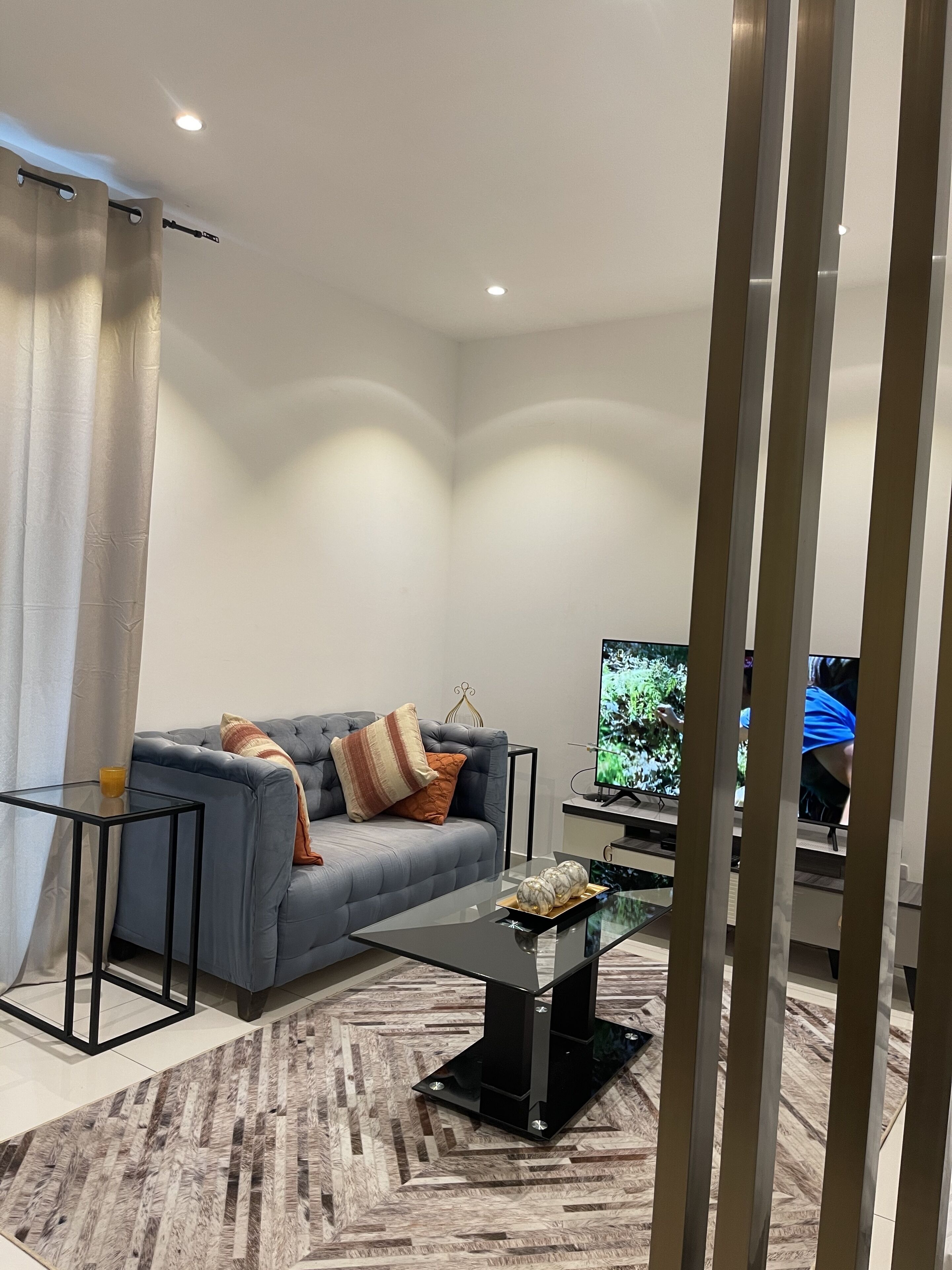 A modern living room with a grey sofa, a glass coffee table, and a flat-screen TV.