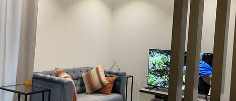 A modern living room with a grey sofa, a glass coffee table, and a flat-screen TV.