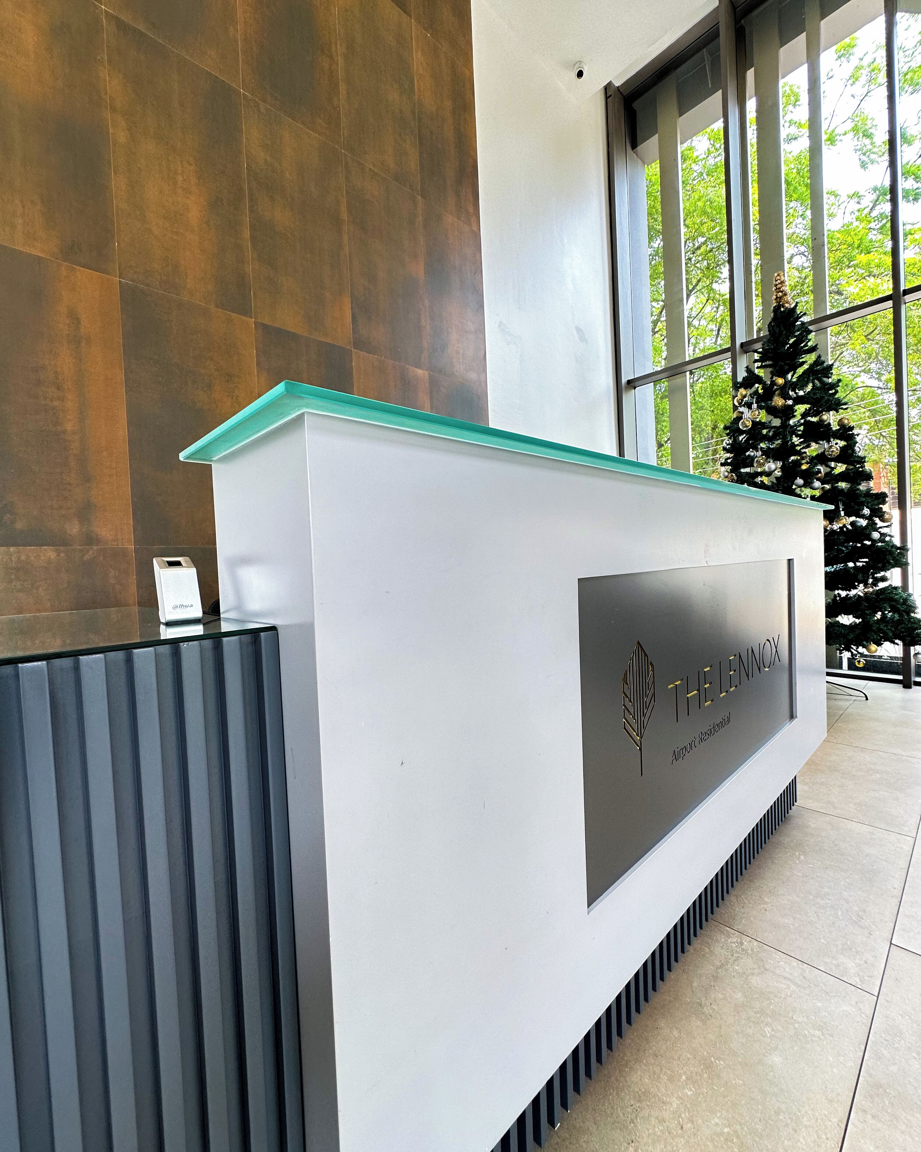 Un mostrador de recepción con un logotipo y nombre, un árbol de Navidad y ventanas grandes al fondo.