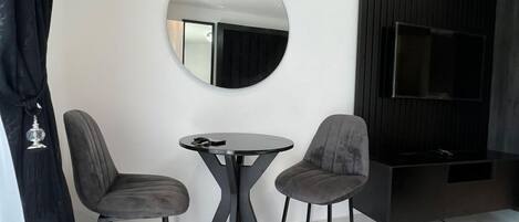 A modern living room with a round mirror, two grey chairs, a small round table, a flat-screen TV, and a built-in entertainment unit.