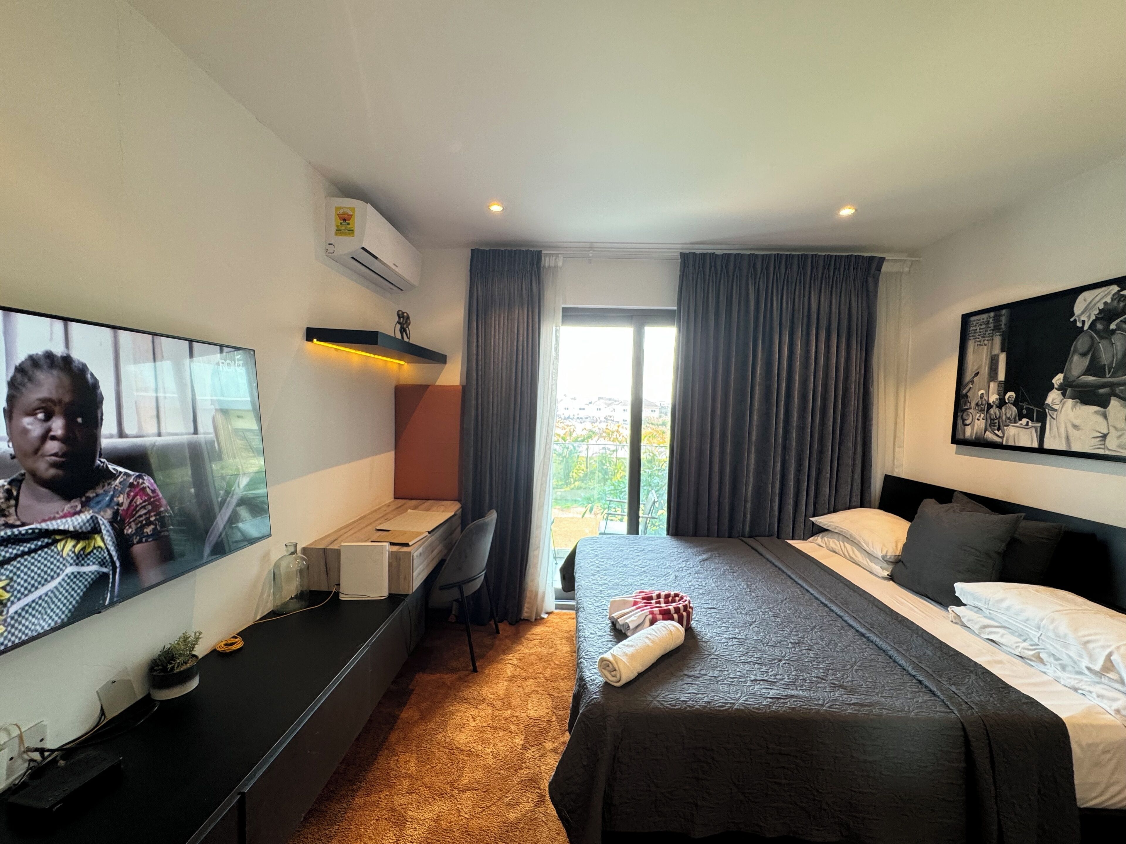 A hotel room with a bed, a desk, a TV, and a large window with curtains.