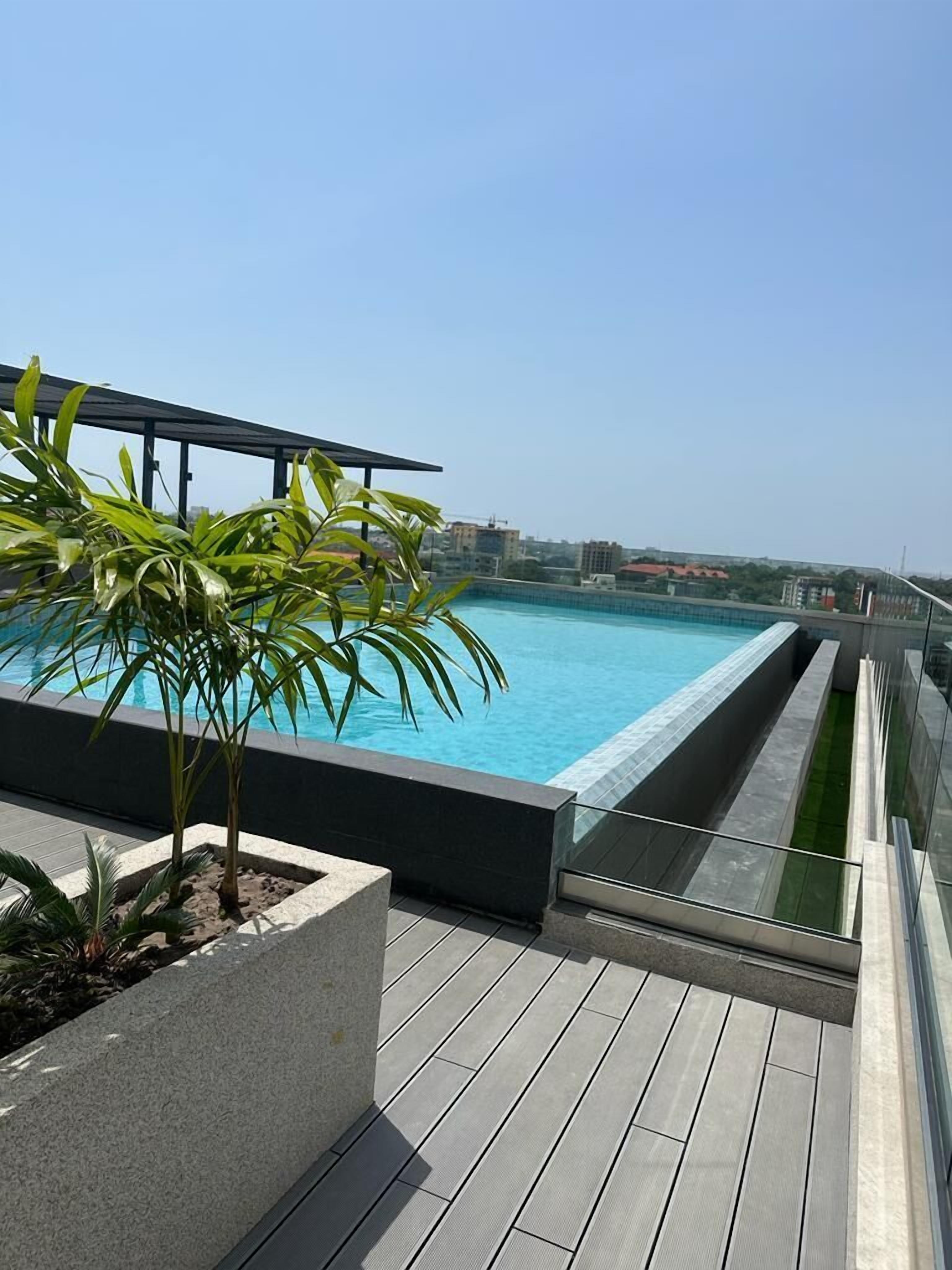 A rooftop pool with clear blue water, surrounded by a wooden deck and potted plants.