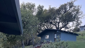 A wooden deck leading to a small cabin with a sloped roof, surrounded by a stone pathway and greenery.
