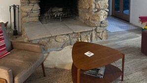 A stone fireplace with a fire, a wooden bench, and a sofa in a living room.