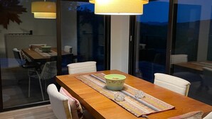 A dining area with a wooden table, white chairs, a yellow pendant light, and a glass door leading outside.