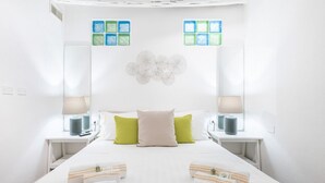 Une chambre d’hôtel avec un grand lit, deux tables de chevet avec des lampes, un élément décoratif mural et une fenêtre donnant sur un beau paysage.