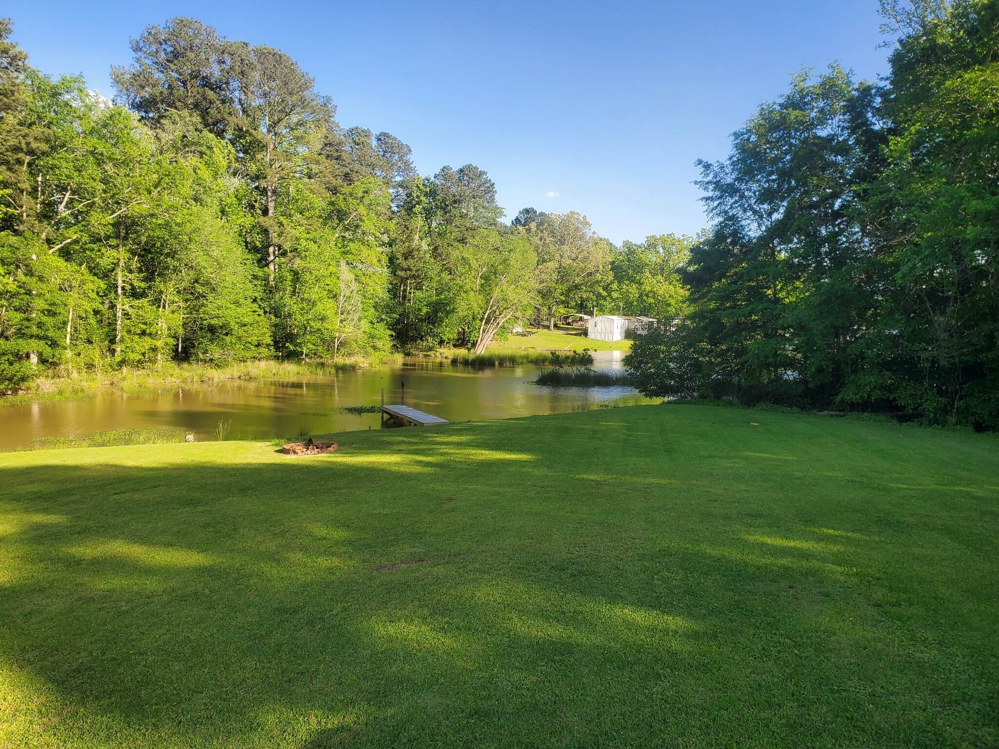 A serene outdoor area with a pond, grassy lawn, and trees.