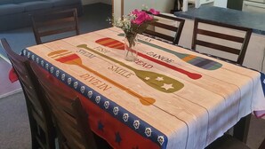 A dining area with a table covered by a tablecloth featuring a fish and canoe design, surrounded by wooden chairs.