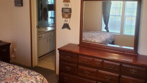 A bedroom with a large mirror, a dresser, a bed with a patterned bedspread, and a sign on the wall.