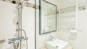 A modern bathroom with a glass-enclosed shower, a white sink, and a mirror with a decorative tile border. - Renovated house and tastefully decorated in La Chaume (Les Sables-d´Olonne)