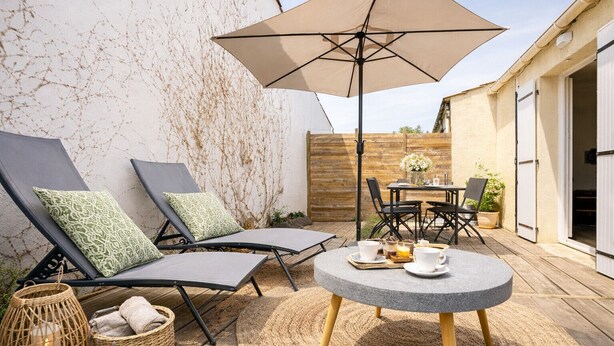 A patio with two lounge chairs, a round table with cups and a candle, and a large umbrella. - Renovated house and tastefully decorated in La Chaume (Les Sables-d´Olonne)