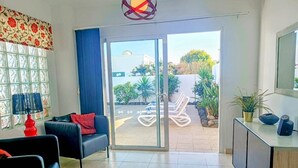 Ein modernes Wohnzimmer mit einer Couch, einer roten Lampe und Blick auf einen Garten durch eine Glastür.