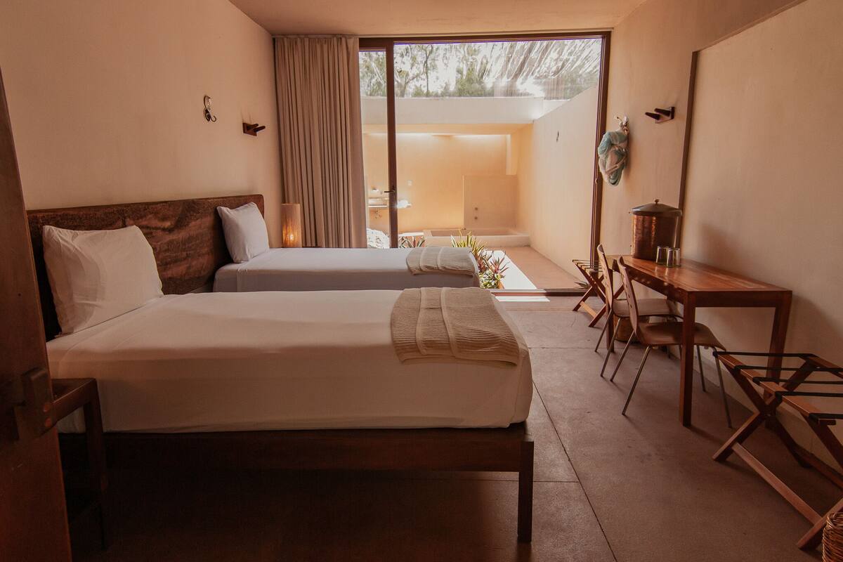 A hotel room with two beds, a desk, and a view of the outdoors.